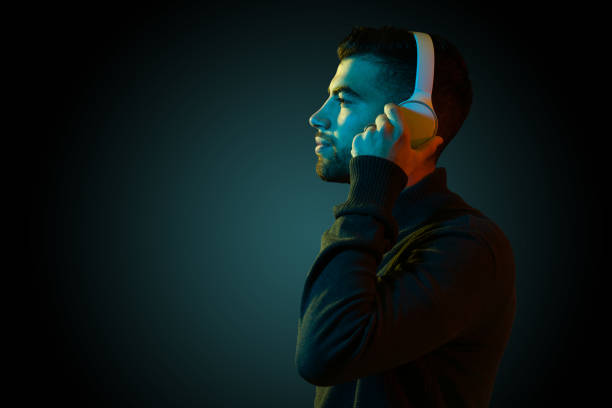 Handsome latin man putting on wireless headphones and listening to relaxing music against a dark modern background with copy space