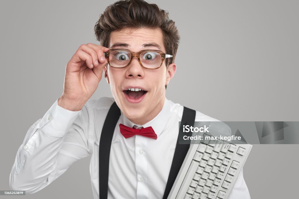 Comic smart developer with keyboard Funny clever male programmer in glasses and with white keypad looking at camera with astonishment on gray background in studio Nerd Stock Photo