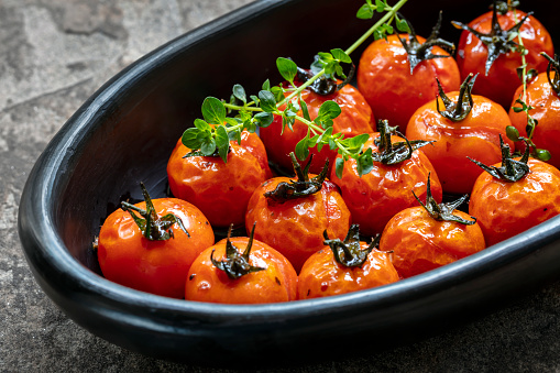 Roasted balsamic cherry tomatoes in black rustic dish on slate.  Topped with thyme.