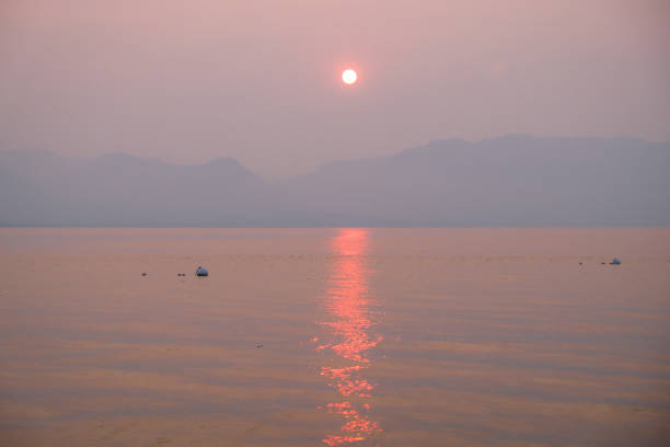 A light haze acts as a beautiful diffuser as the sun sets over the mountain range at Lake Tahoe. The air itself is tinted with a soft pink glow creating a truly magical scene as the pink sunlight reflects in the water and the distant mountain range can be seen in a blue silhouette.