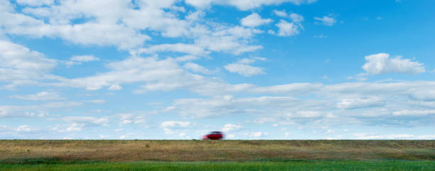 Red car driving on grassland highway.