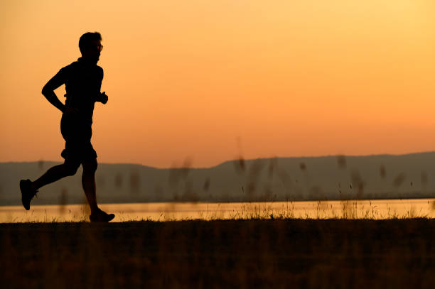 istock a man running Silhouette sunset at lake and Mountain 1365277960