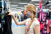 New normal retail shopping. Teenage blond girl wearing face mask choosing sports clothing at sport warehouse retail shop.