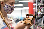 New normal retail shopping. Teenage blond girl wearing face mask choosing walking shoes sandalds at sport warehouse retail shop.