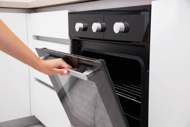 la mano di una donna apre la porta di un forno elettrico a convezione. forno da incasso in cucina, consumo energetico - convection foto e immagini stock