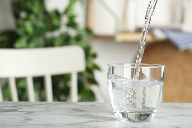 istock Pouring water into glass on white marble table indoors, space for text. Refreshing drink 1365292069
