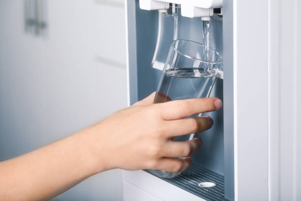 mujer llenando vidrio con enfriador de agua en interiores, primer plano. bebida refrescante - refrigeradora de agua fotografías e imágenes de stock