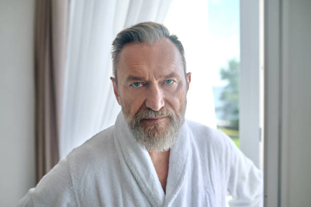 istock Serene mature gentleman in a white terry bathrobe standing indoors 1365295821
