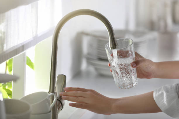 donna che versa l'acqua nel vetro in cucina, primo piano - bicchiere foto e immagini stock