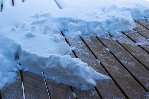 This image shows a full frame abstract texture background of partially shoveled deep snow on a cedar wood deck.