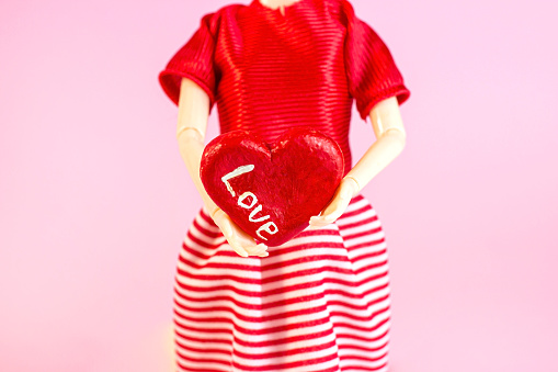 Woman doll holding a heart with Love word on light pink background. Valentines day celebration concept.