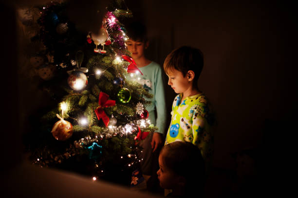 istock Kids looking on Christmas tree with shining garlands on evening home. 1365298504