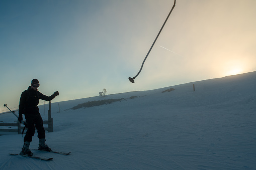 A young man on skis lets go of the pole at the top of the ski lift in the fog