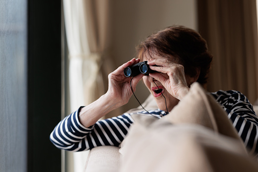 Senior woman looking through binoculars looking excited.