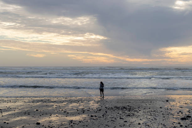 Oceanside, OR, USA - Jan 16, 2022: A young woman runs from wave during sunset on the beach in Oceanside, Oregon. Pacific tsunami threat recedes as volcano ash over Tonga hinders response.