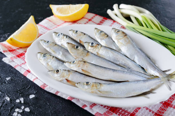 istock Fresh sea small fish on a plate on a concrete background. Sardines ready for cooking with lemon, coarse sea salt and green onion. 1365309046