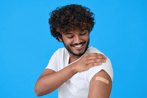 istock Happy young indian man showing bandage on arm after getting vaccination on blue. 1365310324