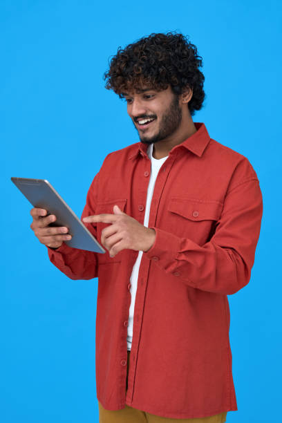 istock Happy indian young man using digital tablet isolated on blue background. 1365310326