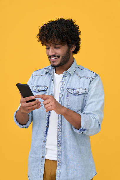 istock Happy indian young man using cell phone isolated on yellow background. 1365310334