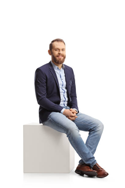 istock Young professional man sitting on a white cube and smiling 1365310648