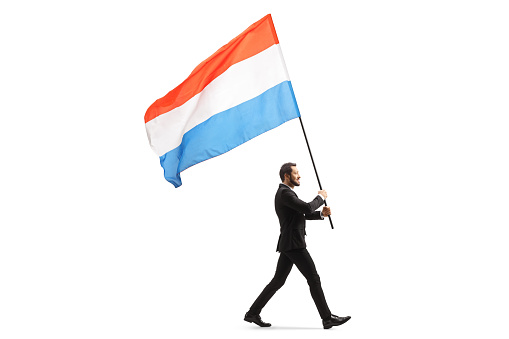 Full length profile shot of an elegant man in a suit walking and carrying a dutch flag isolated on white background