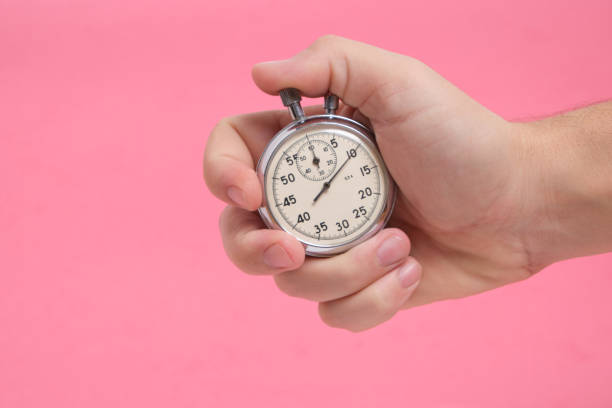 istock Man hand holding stopwatch on pink background. 1365311157