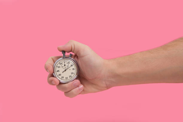 istock Man hand holding stopwatch on pink background. 1365311160