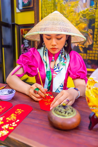 Ho Chi Minh city, Vietnam - 17 Jan 2022: Beautiful Vietnamese scholar writes calligraphy at lunar new year. Calligraphy festival is a popular tradition during Tet holiday in Vietnam