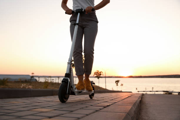 istock Woman riding electric kick scooter outdoors at sunset, closeup 1365315521