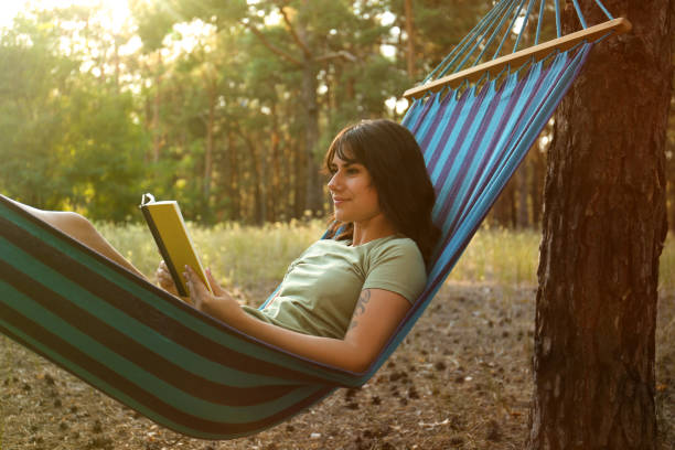 istock Woman with book resting in comfortable hammock outdoors 1365315836