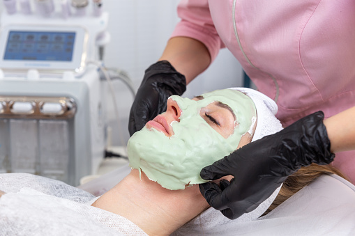 Beautician removes a clay mask from the face of a young woman in the Spa salon. Beautiful young girl at the beautician does the spa procedures