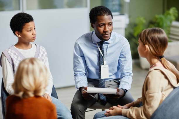 Therapy Session for Children Portrait of young African-American psychologist listening to children in support group circle mental health professional stock pictures, royalty-free photos & images