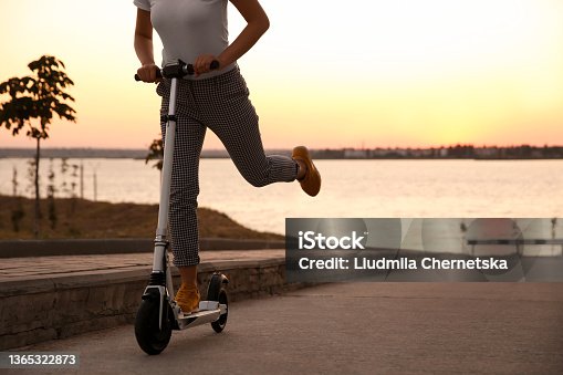 istock Woman riding electric kick scooter outdoors at sunset, closeup 1365322873