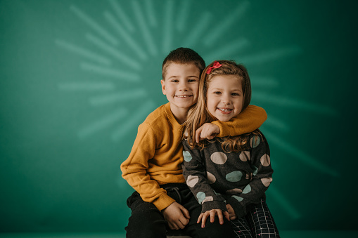 Brother embracing his smiling sister while they standing in front of green background