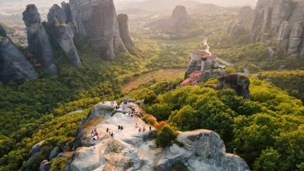 Aerial drone view of the Meteora in Greece at sunset. Rock formations with viewpoint full of people and monastery. A lot of greenery, sacred place Aerial drone view of the Meteora in Greece at sunset. Rock formations with viewpoint full of people and monastery. A lot of greenery, sacred place