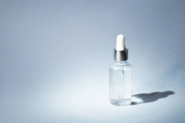 istock Transparent glass bottle with silver and white pipette in light on grey background mockup. Facial serum in dropper bottle for branding closeup. Minimal concept. Copy space, front view 1365327475
