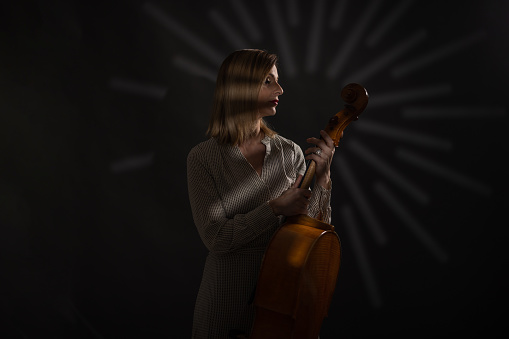 Woman in dress standing in studio and holding cello