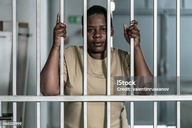 Young Afro Woman Looking Serious And Desperate Behind Bars Which May Be Prison Bars Or Those Of A Security Gate Stock Photo - Download Image Now