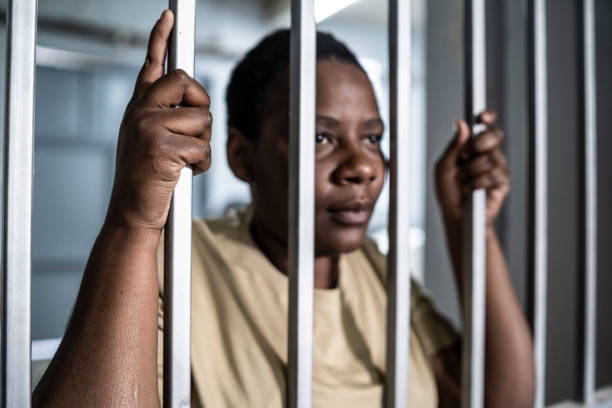 istock Young afro woman looking  serious and desperate   behind bars which may be prison bars or those of a security gate 1365328015