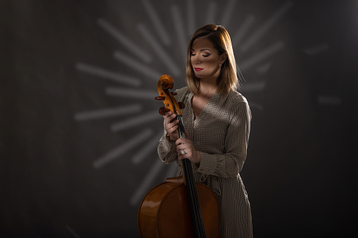 Woman in dress standing in studio and holding cello
