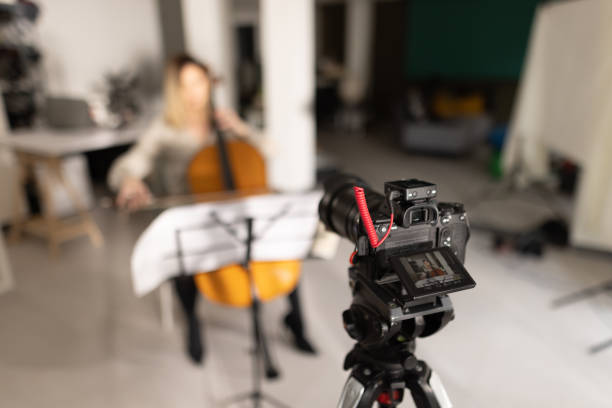 istock Camera standing on tripod while woman sitting and playing cello in background 1365329337