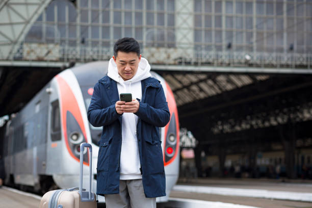 istock Asian tourist booking accommodation at home using mobile phone, passenger arrives by train to new city 1365333970