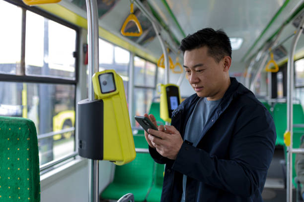대중 교통에서 행복하고 성공적인 아시아 남성 승객은 미소를 짓고 카메라를보고 휴대 전화를 사용하여 티켓을 샀다. - bus commuter passenger mobile phone 뉴스 사진 이미지