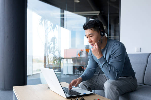 istock portrait of an Asian call center employee, man working with headset and computer, remote work, video call, online help 1365334131