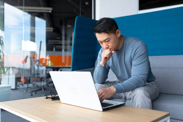 istock A thinking Asian man works at a computer in a modern office, a freelancer is focused on solving a task, makes an important job. 1365334209