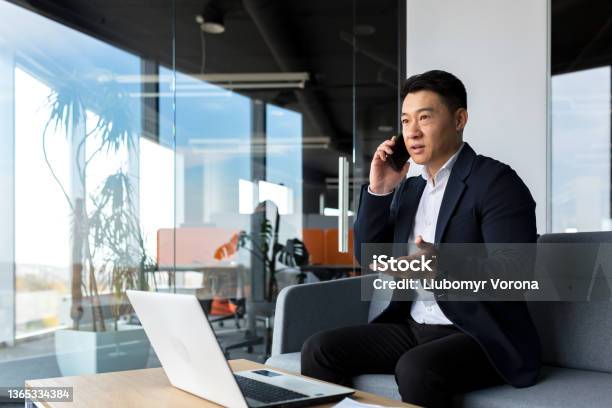 Thinking Asian Businessman Businessman Talking On The Phone Working In A Modern Office Listening Seriously Stock Photo - Download Image Now