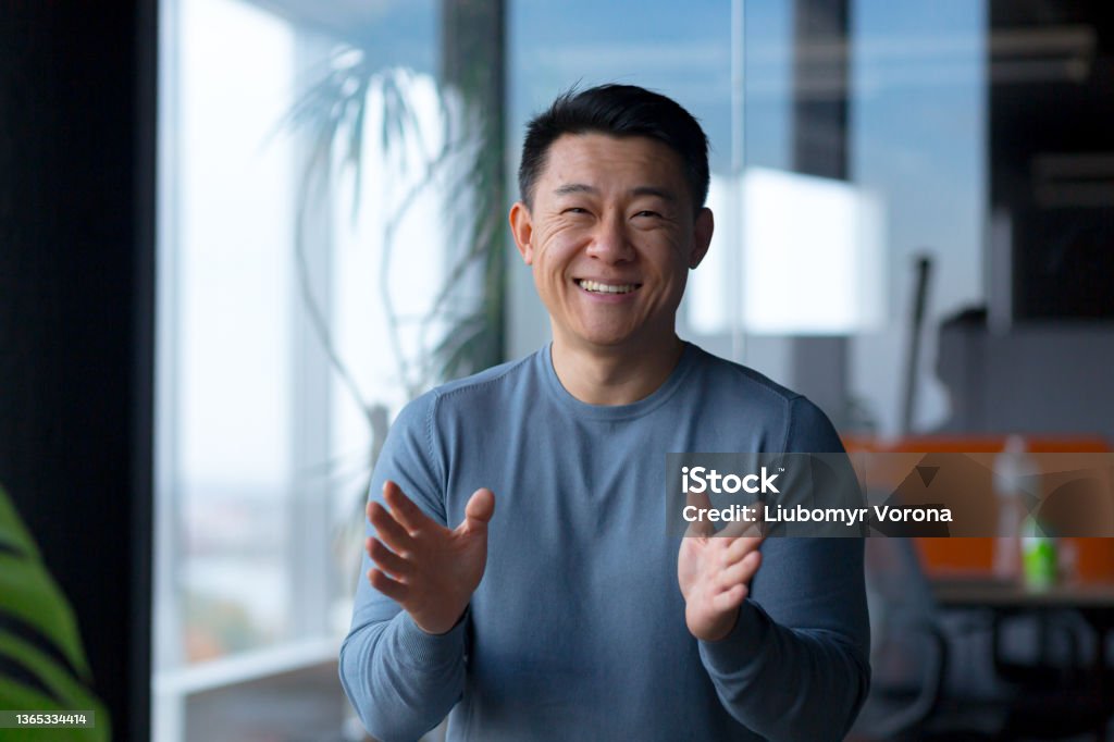 Portrait of a cheerful employee, looking at the camera and gesturing with his hands, Asian communicates on a video call, looks at the webcam Discussion Stock Photo