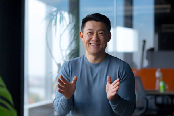 Portrait of a cheerful employee, looking at the camera and gesturing with his hands, Asian communicates on a video call, looks at the webcam Portrait of a cheerful employee, looking at the camera and gesturing with his hands, Asian communicates on a video call, looks at the webcam webcam stock pictures, royalty-free photos & images