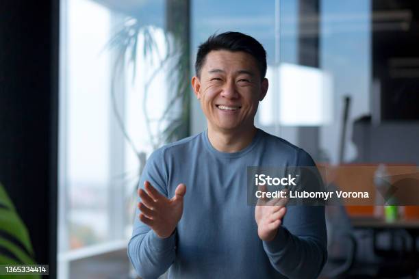 Portrait Of A Cheerful Employee Looking At The Camera And Gesturing With His Hands Asian Communicates On A Video Call Looks At The Webcam Stock Photo - Download Image Now