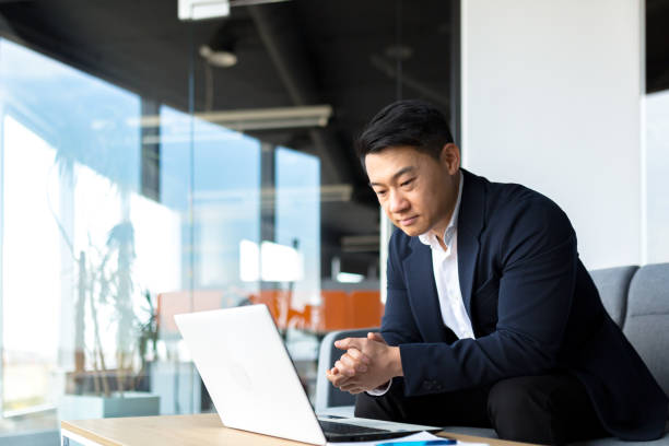 istock Portrait thoughtful Asian businessman working on a laptop computer at a modern office desk. Confident Focused pensive man in formal suit indoors. thinking of inspiration solving a problem. Startup 1365334475
